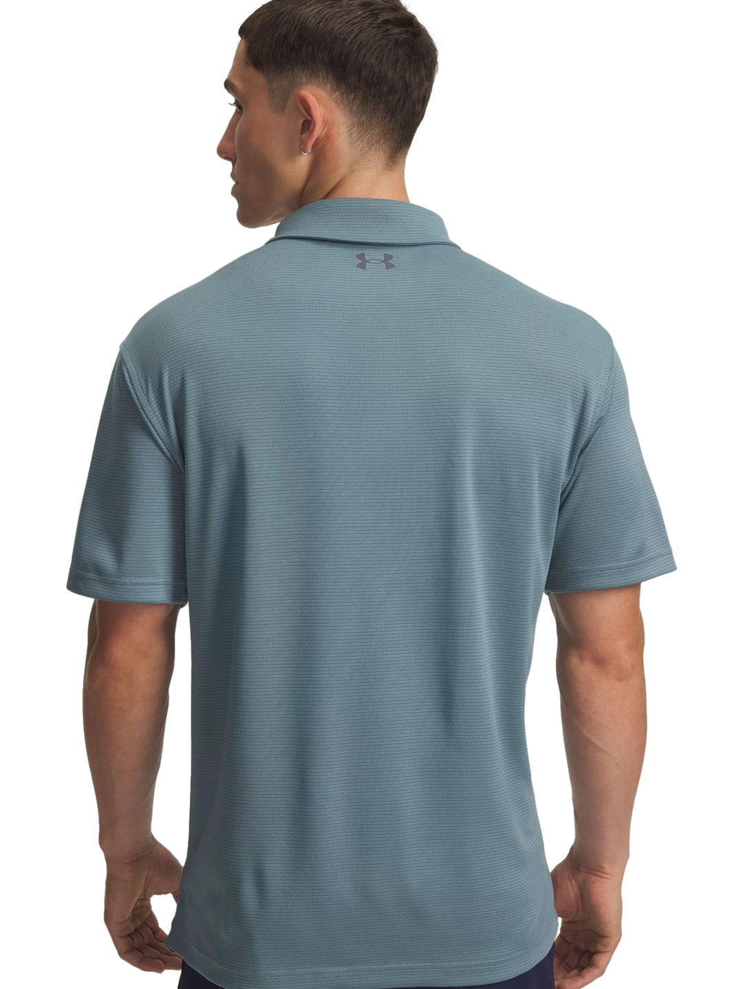 Hombre vistiendo una playera polo deportiva de color azul con logo de Under Armour en el pecho.