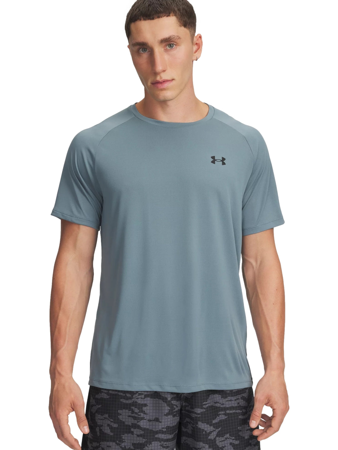 Hombre vistiendo una camiseta deportiva de manga corta color azul grisáceo de la marca Under Armour.