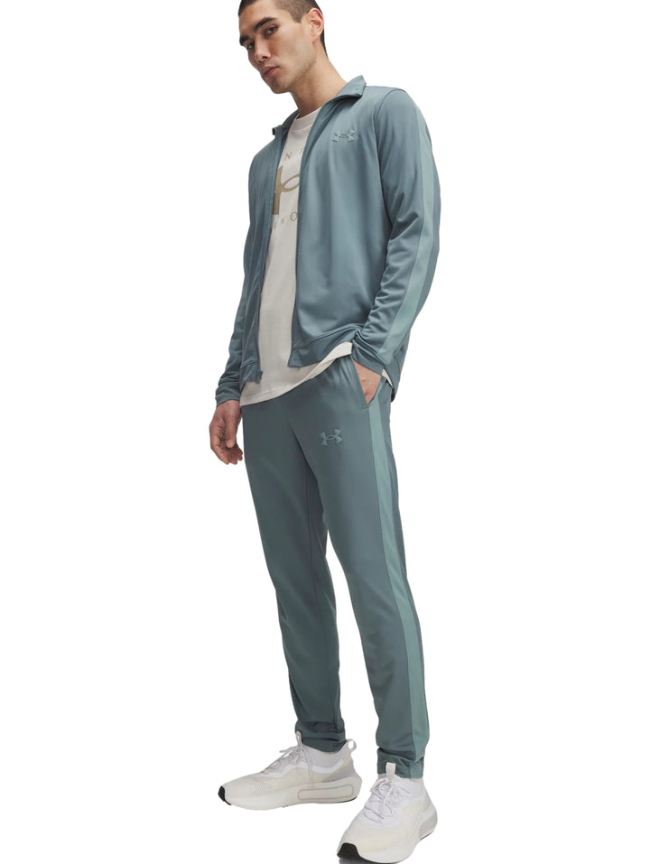Hombre vistiendo un conjunto deportivo Under Armour de color azul grisáceo compuesto por chaqueta y pantalón.