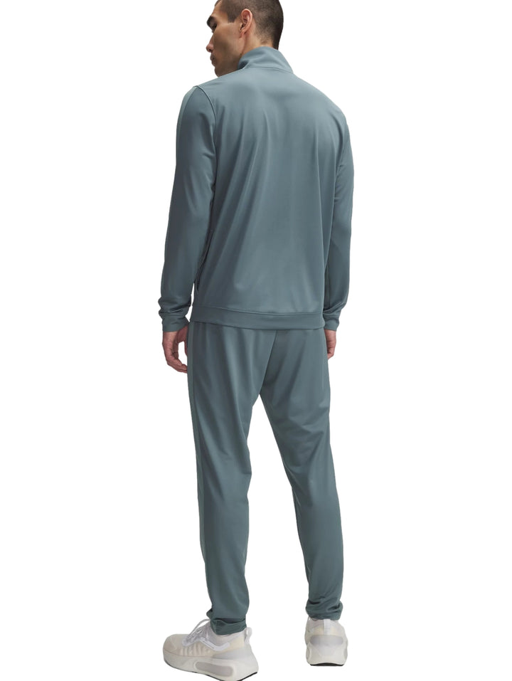 Hombre vistiendo un conjunto deportivo Under Armour de color azul grisáceo compuesto por chaqueta y pantalón.