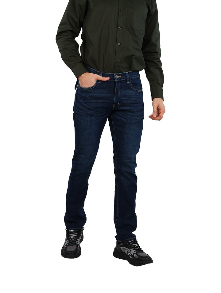 Hombre vistiendo pantalones jeans azul oscuro de corte recto con camisa verde y calzado negro.