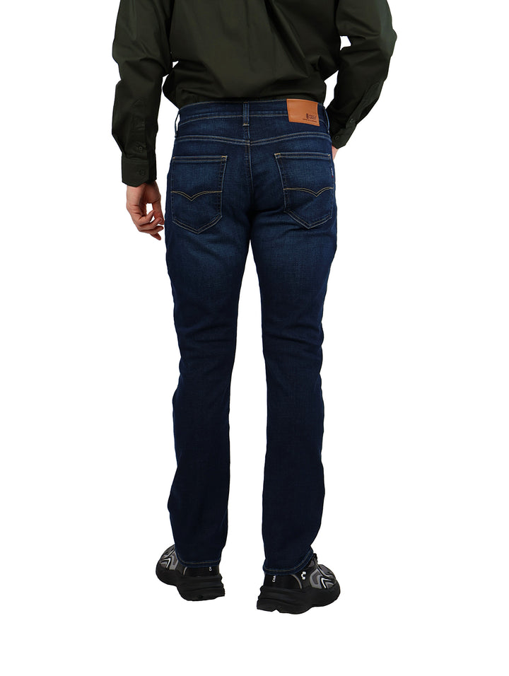 Hombre vistiendo pantalones jeans azul oscuro de corte recto con camisa verde y calzado negro.