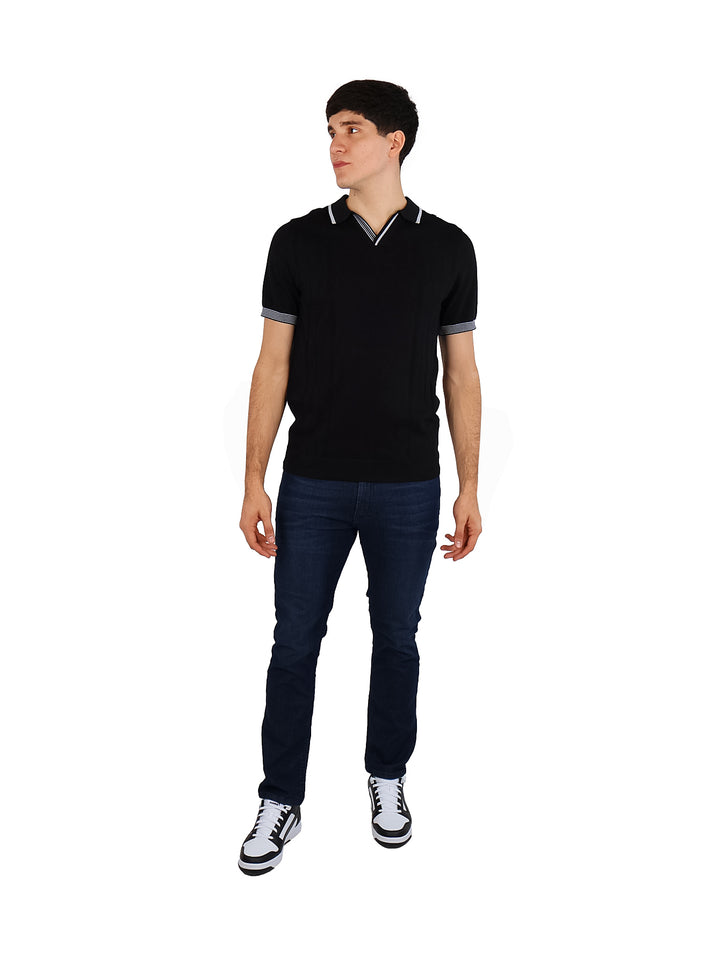 Hombre vistiendo playera polo tejida color negro con detalles blancos en el cuello y los bordes de las mangas.