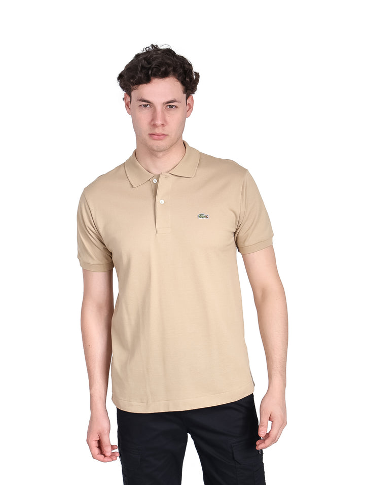Hombre vistiendo una playera polo de color beige de la marca Lacoste con cuello y manga corta.