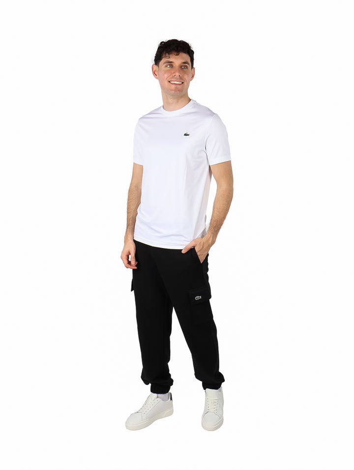 Hombre vistiendo una playera blanca de manga corta y cuello redondo de la marca Lacoste.