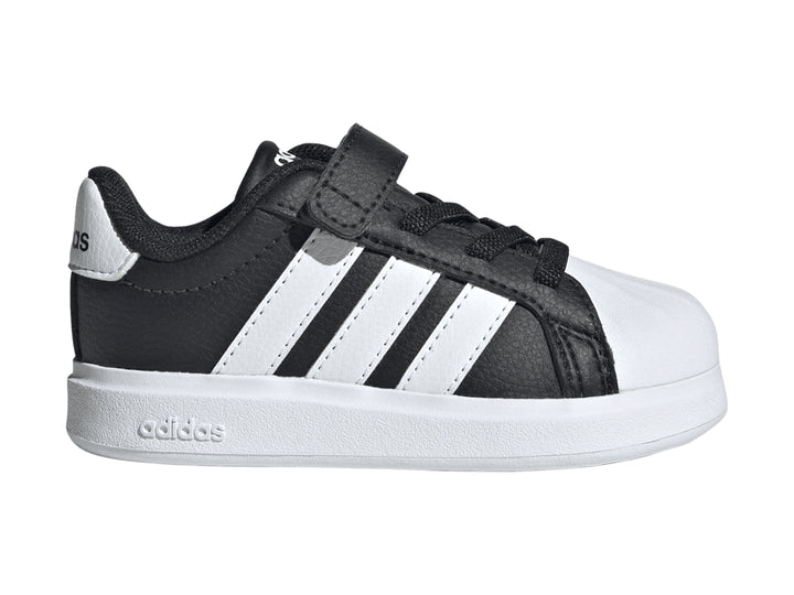 Tenis Adidas negros con tres franjas blancas, cierre de velcro y suela blanca.