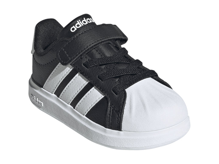 Tenis Adidas negros con tres franjas blancas, cierre de velcro y suela blanca.