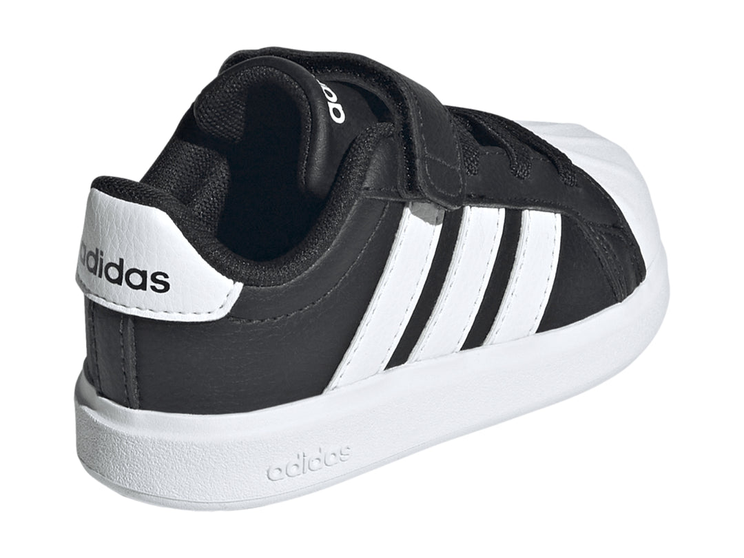 Tenis Adidas negros con tres franjas blancas, cierre de velcro y suela blanca.