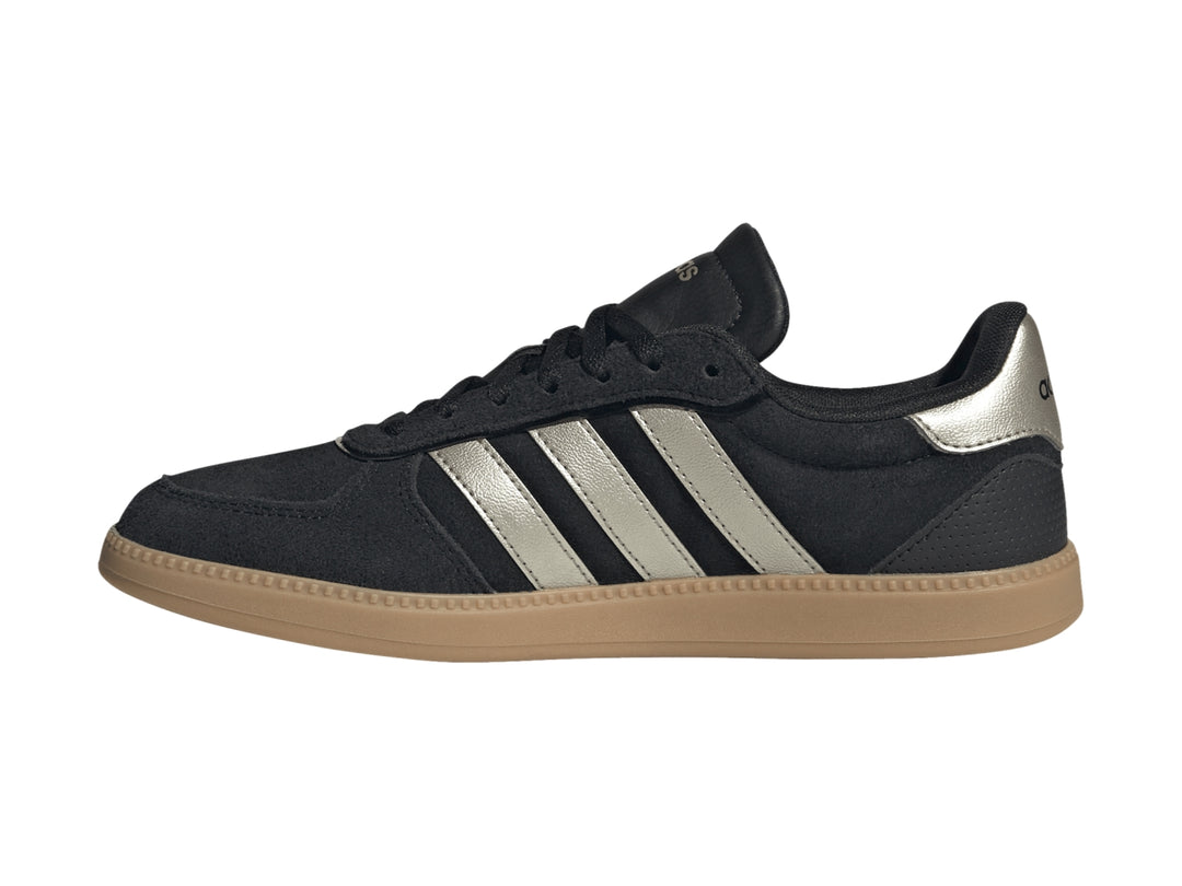 Tenis Adidas negros con tres franjas plateadas metálicas y suela de goma color caramelo.