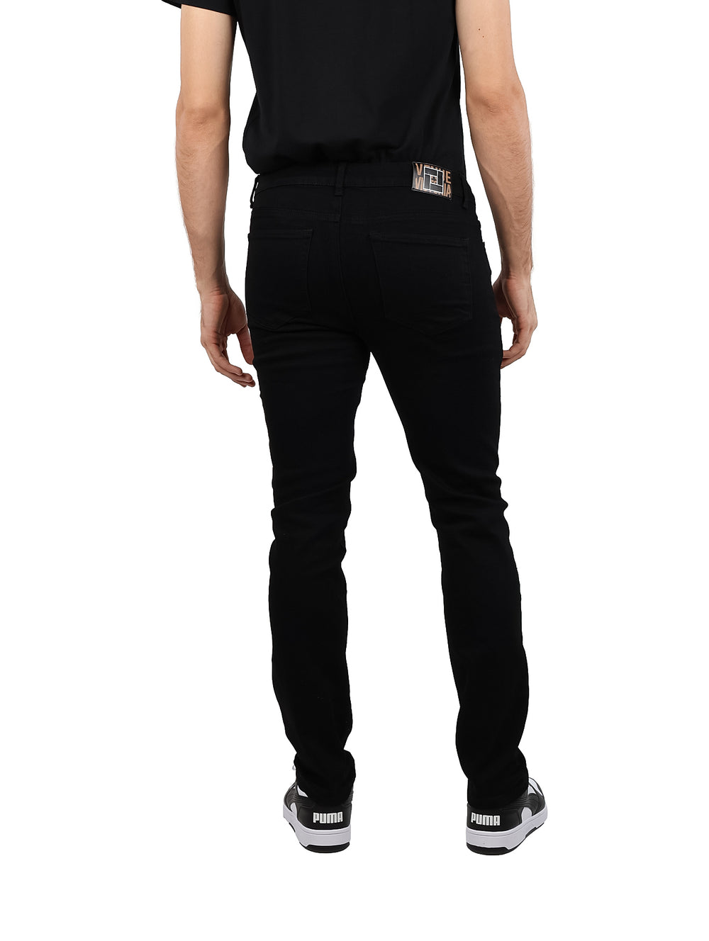 Hombre vistiendo jeans negros de corte ajustado y camiseta negra sobre fondo blanco.