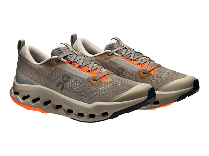 Tenis deportivos On Cloudsurfer Trail 2 color gris topo con detalles naranjas y suela con tecnología CloudTec.
