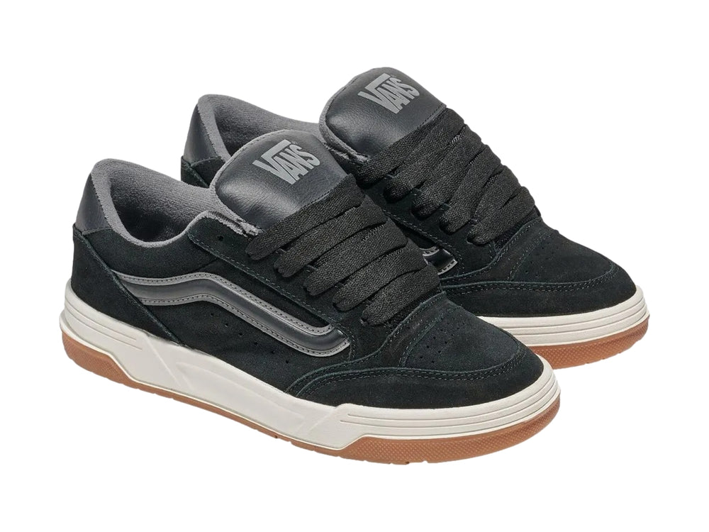Tenis Vans negros con franja gris, entresuela blanca y suela de goma color caramelo.
