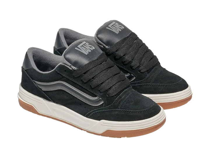Tenis Vans negros con franja gris, entresuela blanca y suela de goma color caramelo.