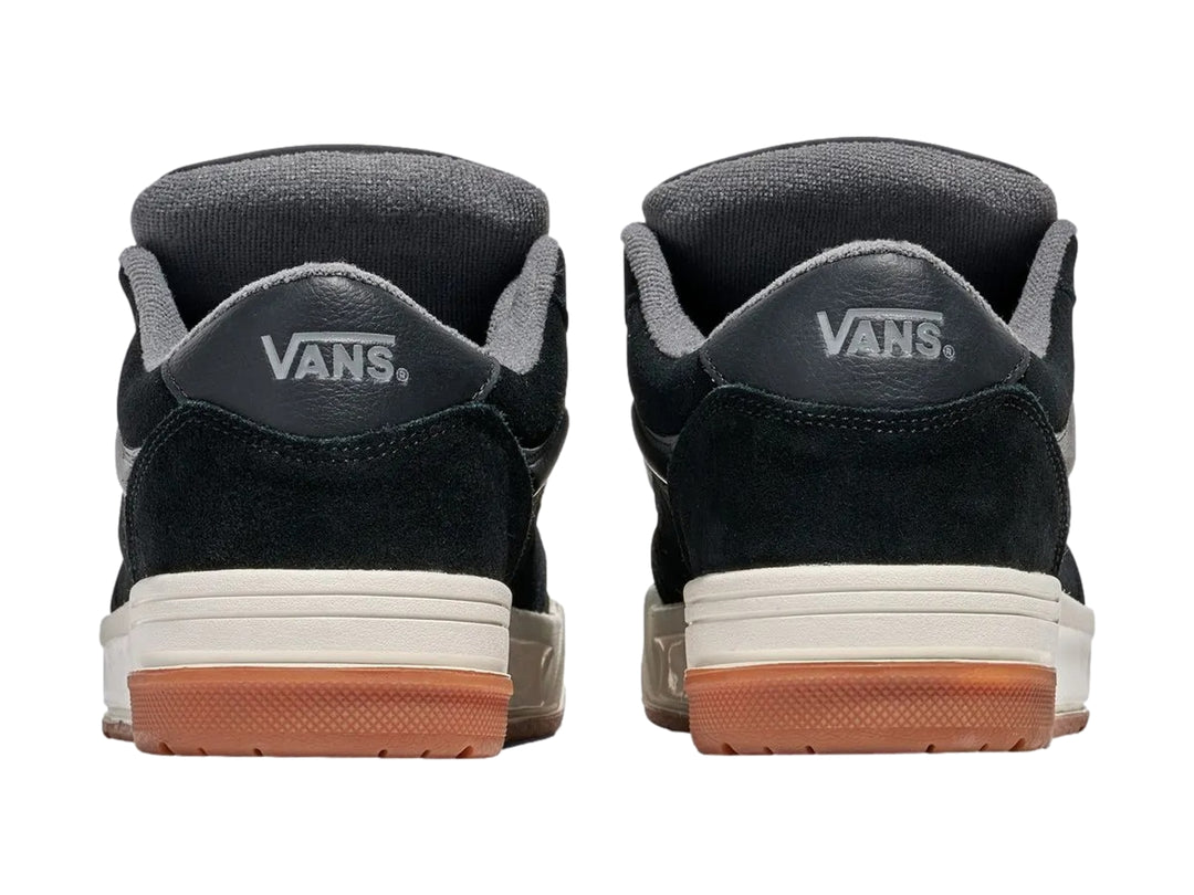Tenis Vans negros con franja gris, entresuela blanca y suela de goma color caramelo.