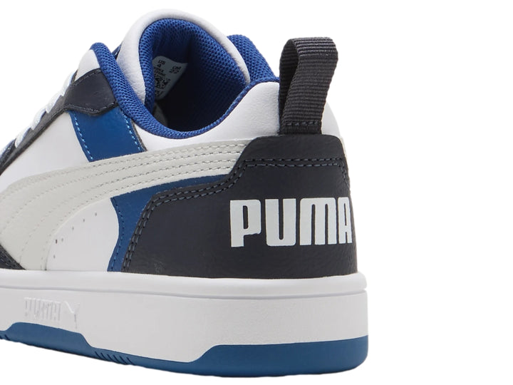 Tenis PUMA Rebound V6 Lo JR color blanco con detalles en azul y negro, diseño deportivo de corte bajo.