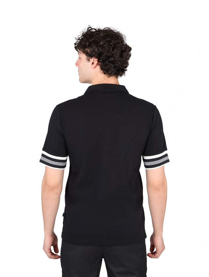 Hombre vistiendo playera polo negra con cierre y rayas blancas y grises en las mangas.