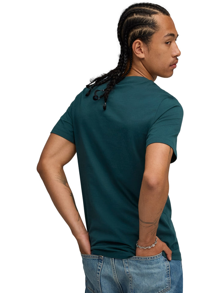 Hombre vistiendo una playera PUMA de color verde terrain con logotipo blanco en el pecho.