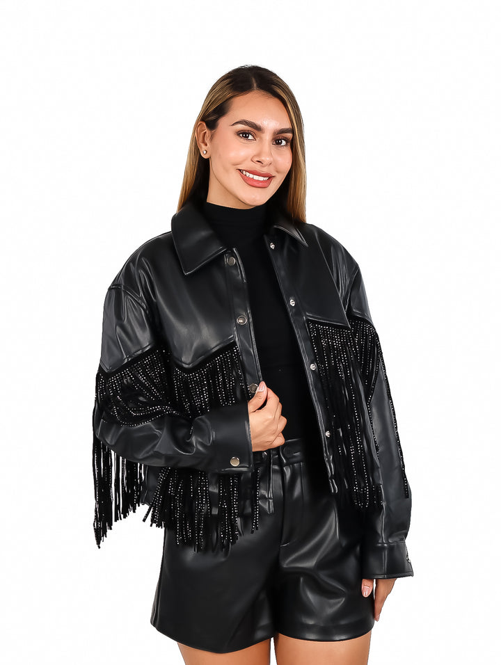 Mujer vistiendo chaqueta de vinipiel negra con flecos laterales y botones frontales.