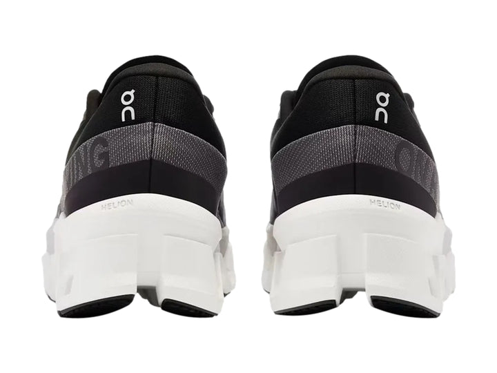 Tenis deportivos On Cloudmonster 2 color negro con suela blanca gruesa y diseño moderno.