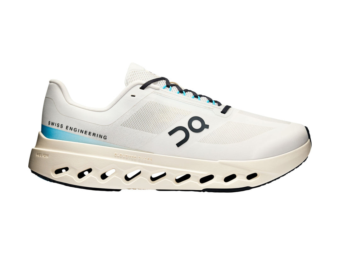 Tenis deportivos On Cloud color ivory con detalles en azul y suela blanca con perforaciones.