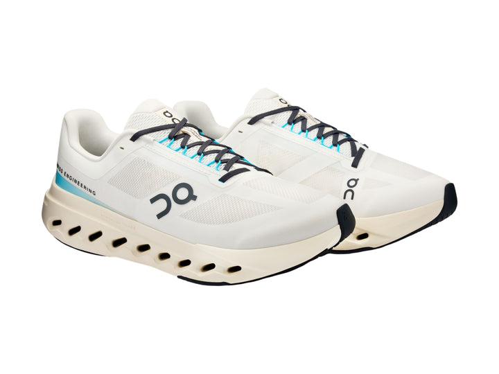 Tenis deportivos On Cloud color ivory con detalles en azul y suela blanca con perforaciones.
