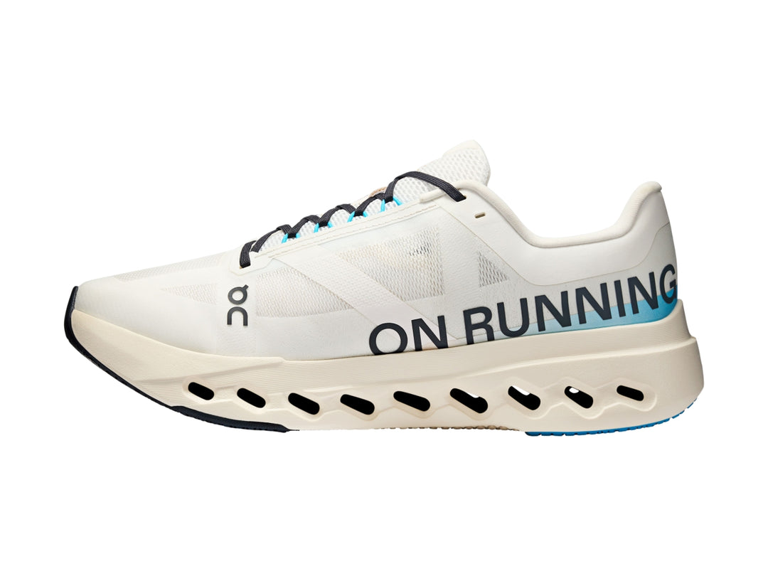 Tenis deportivos On Cloud color ivory con detalles en azul y suela blanca con perforaciones.