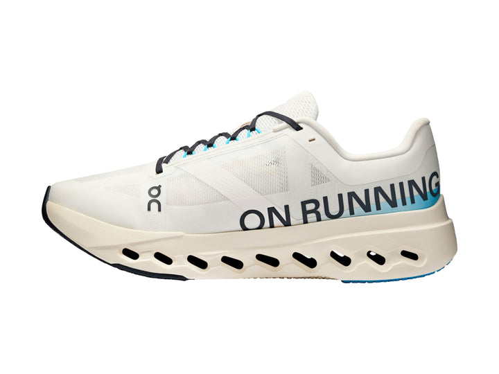 Tenis deportivos On Cloud color ivory con detalles en azul y suela blanca con perforaciones.