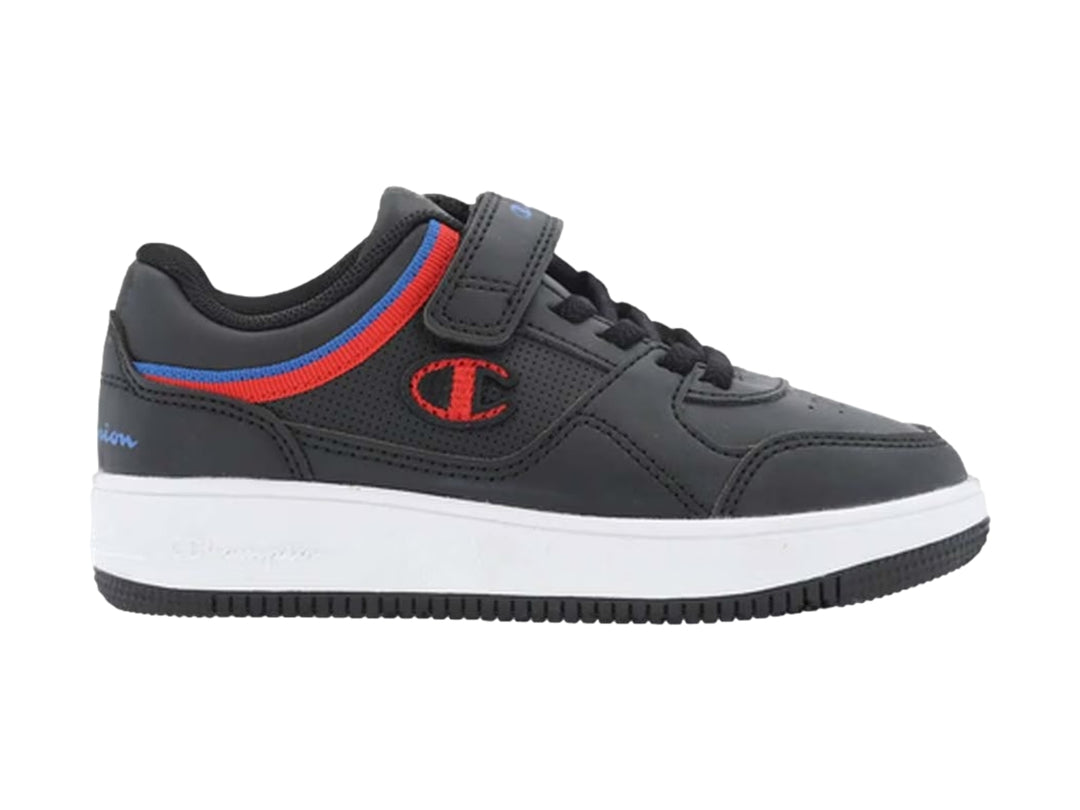 Tenis Champion negros con suela blanca, detalles en rojo y azul, y correa de ajuste.
