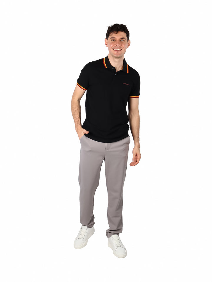 Hombre vistiendo polo negro de Givenchy con detalles de rayas coloridas en el cuello y los bordes de las mangas.