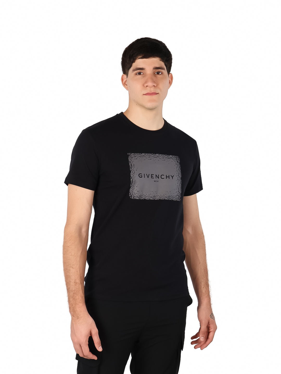 Hombre vistiendo una camiseta negra de manga corta con un estampado cuadrado gris de Givenchy en el pecho.