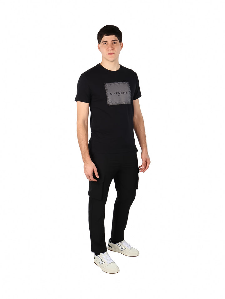 Hombre vistiendo una camiseta negra de manga corta con un estampado cuadrado gris de Givenchy en el pecho.