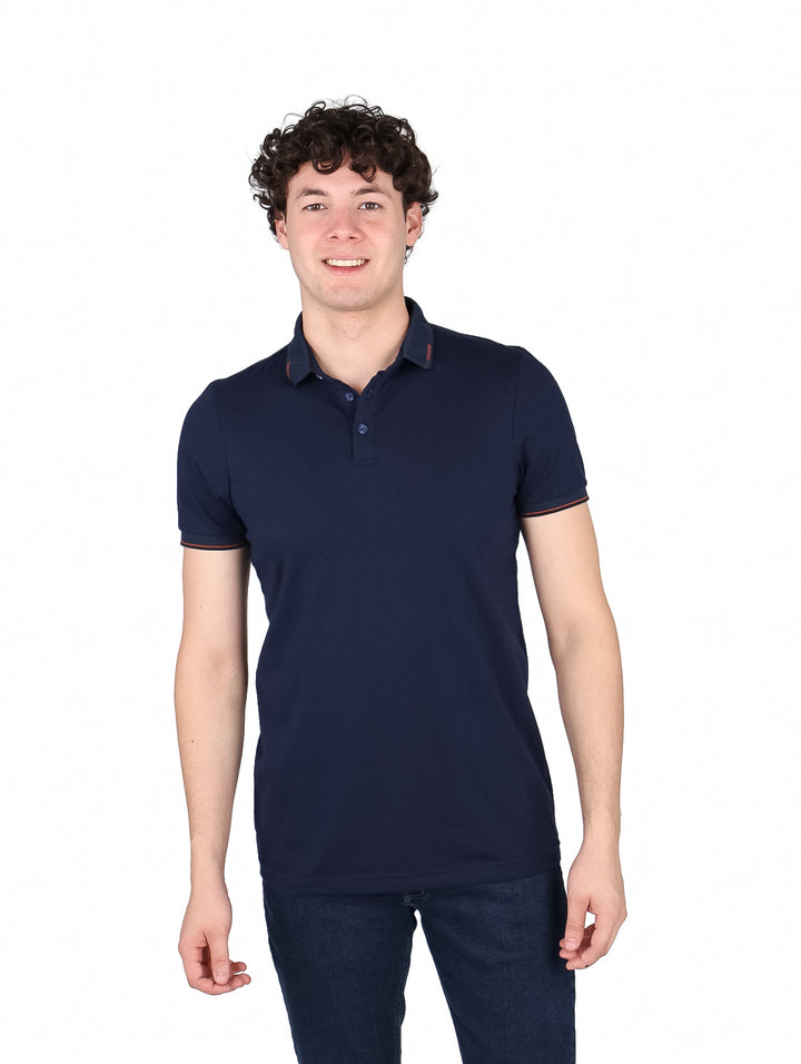 Hombre vistiendo una playera polo color marino con detalles rojos en el cuello y mangas.