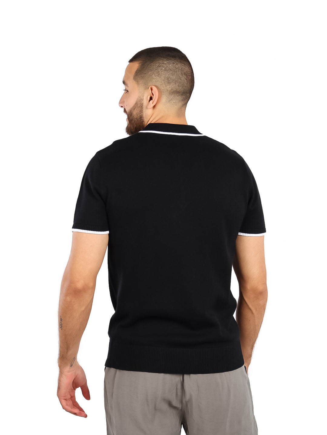 Hombre vistiendo polo negro de tejido con detalles blancos en el cuello y mangas.