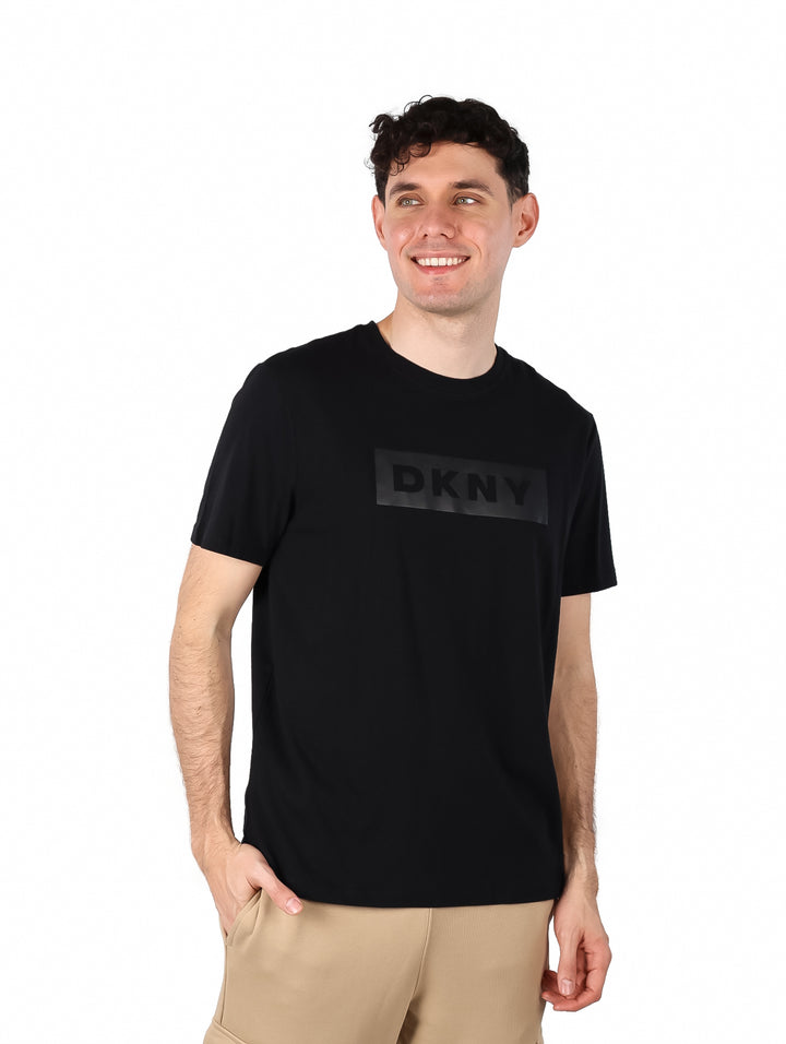 Hombre vistiendo una camiseta negra de manga corta con logotipo DKNY en el pecho.