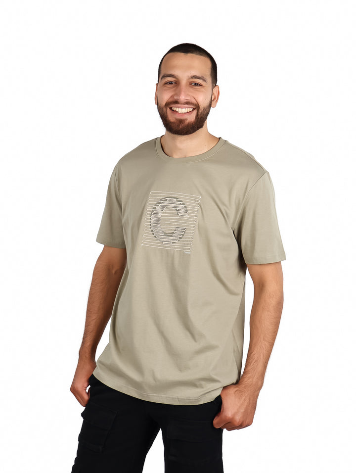 Hombre vistiendo playera Carven color kaki de manga corta con diseño gráfico frontal y pantalones negros.