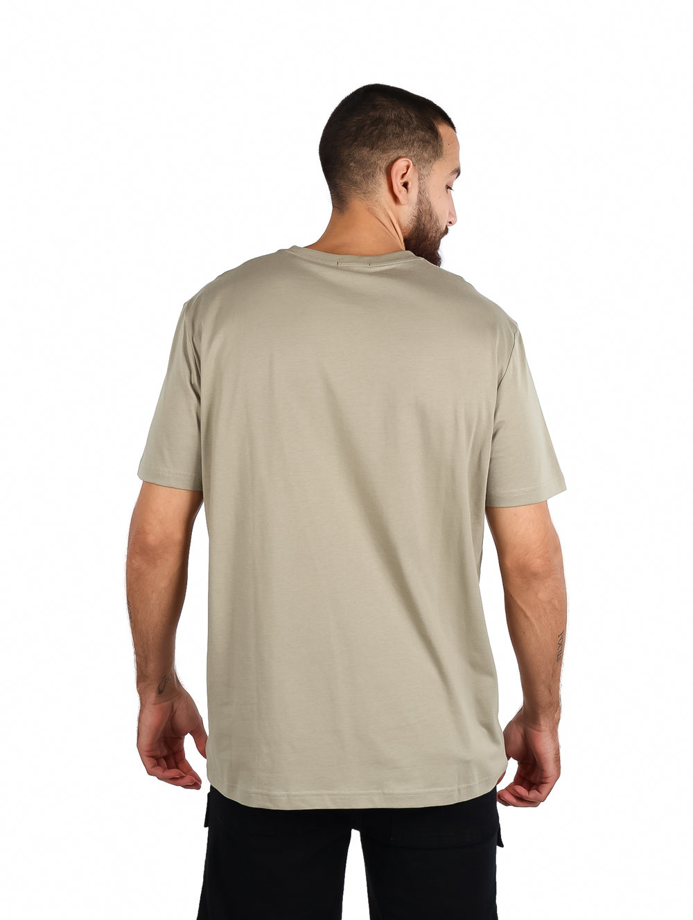 Hombre vistiendo playera Carven color kaki de manga corta con diseño gráfico frontal y pantalones negros.
