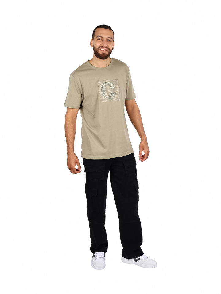 Hombre vistiendo playera Carven color kaki de manga corta con diseño gráfico frontal y pantalones negros.