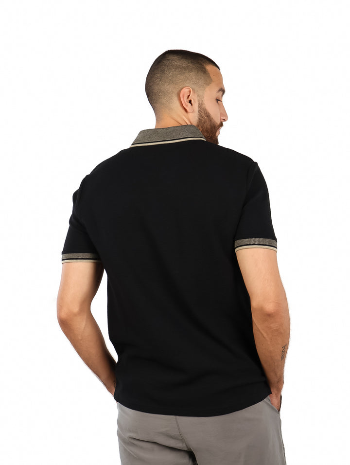 Hombre vistiendo playera polo negra de manga corta con detalles grises en el cuello y puños.