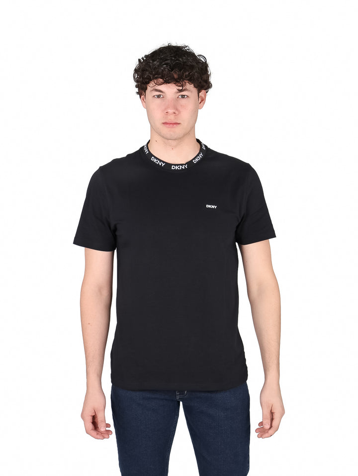 Hombre vistiendo camiseta negra de manga corta DKNY con logotipo blanco en el cuello y pecho.
