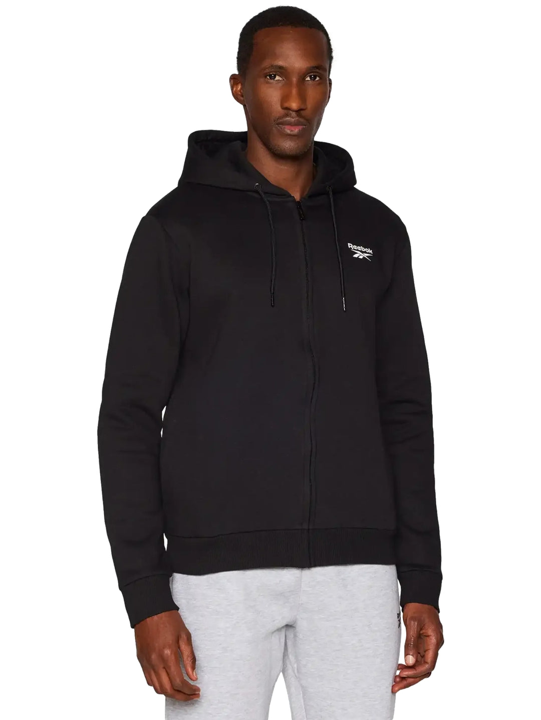 Hombre vistiendo una sudadera negra con capucha y cierre frontal de la marca Reebok.