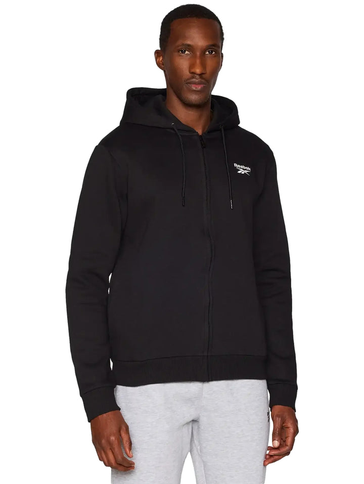 Hombre vistiendo una sudadera negra con capucha y cierre frontal de la marca Reebok.
