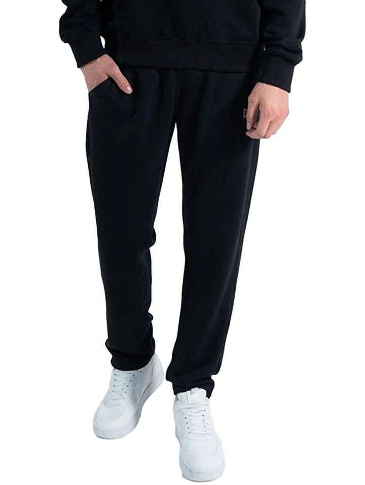 Hombre vistiendo un pantalón deportivo Everlast de color negro con calzado blanco sobre fondo blanco.