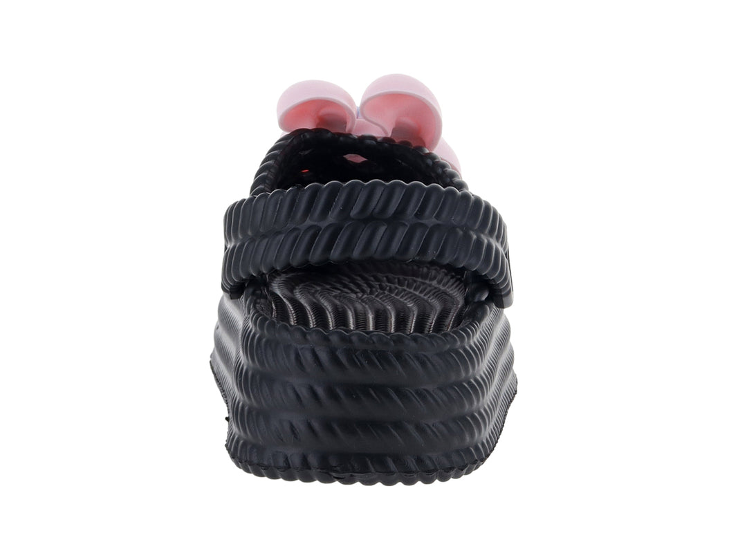 Sandalias tipo clog color negro para niña con detalle decorativo en color rosa.