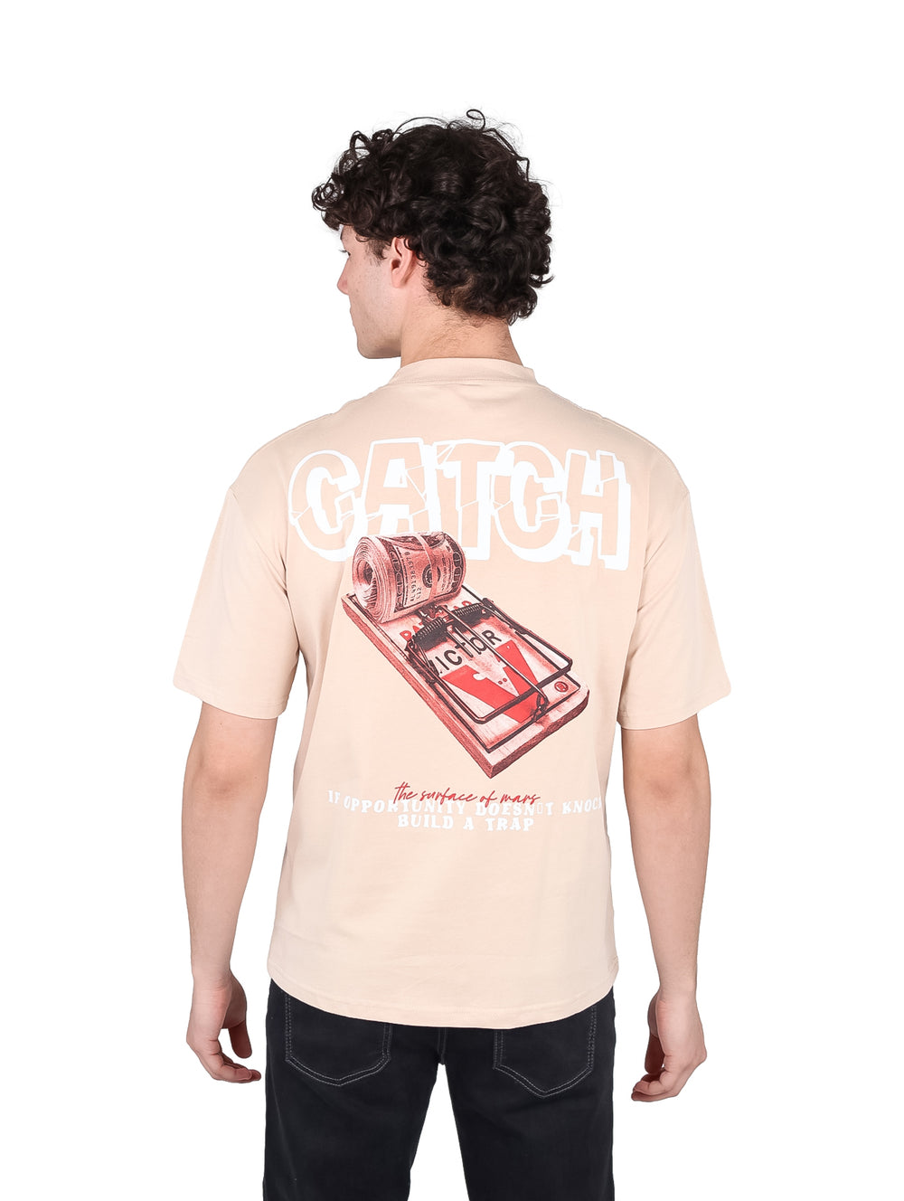 Hombre vistiendo playera oversize color beige con estampado frontal 'CATCH' y cuello redondo.