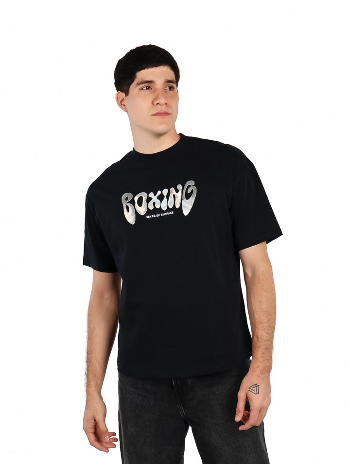 Hombre vistiendo playera oversize color negro con estampado blanco de la palabra BOXING en el pecho.