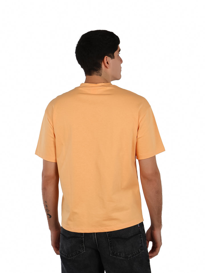 Hombre vistiendo playera oversize color anaranjado con estampado gráfico en el pecho.