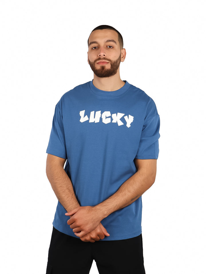 Hombre vistiendo playera azul over size de manga corta con la palabra LUCKY en blanco en el pecho.