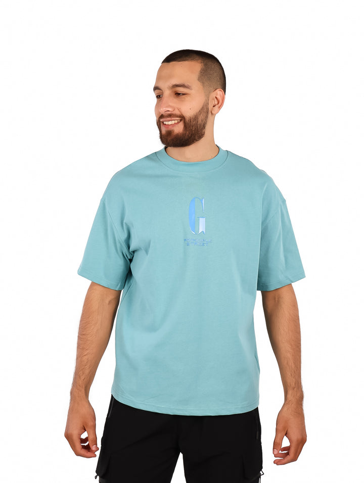 Hombre vistiendo playera oversize de color azul claro con un logotipo discreto en el pecho.