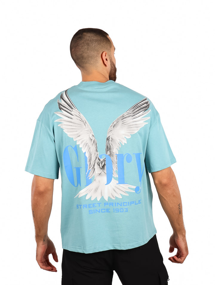 Hombre vistiendo playera oversize de color azul claro con un logotipo discreto en el pecho.