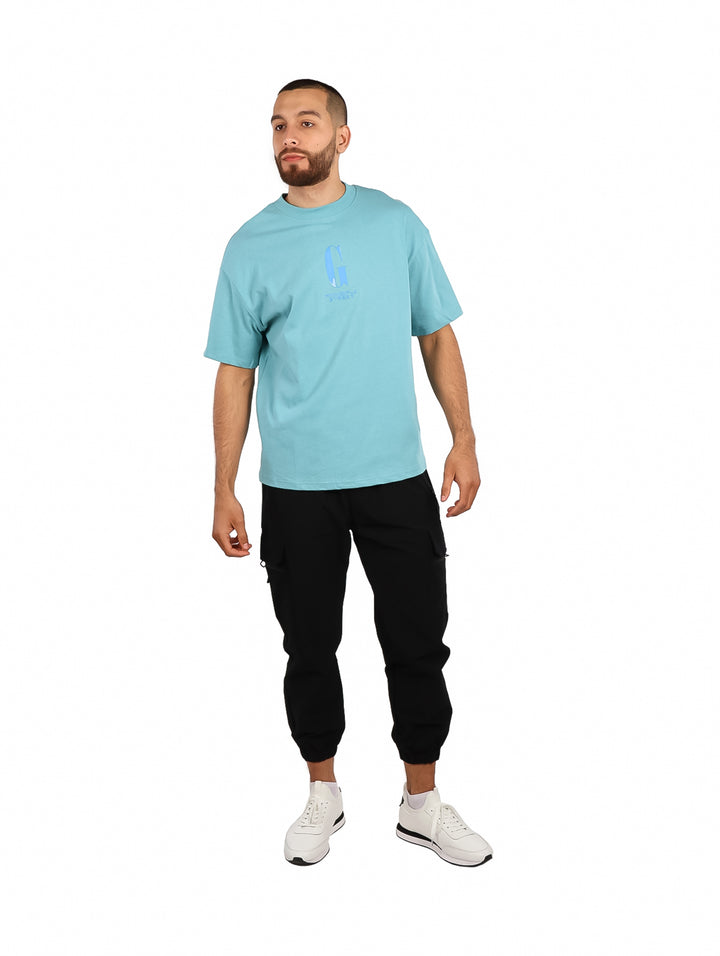 Hombre vistiendo playera oversize de color azul claro con un logotipo discreto en el pecho.